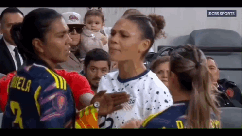 Two Female Soccer Players Talking With Baby in Background