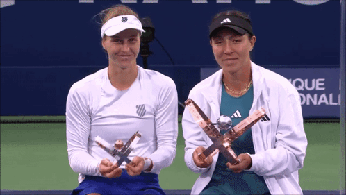 two female tennis players holding trophies in front of a sign that says que