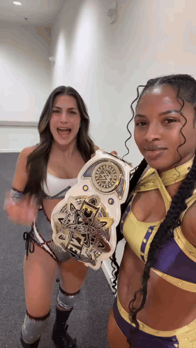 two female wrestlers are posing for a picture while holding a wwe championship belt .