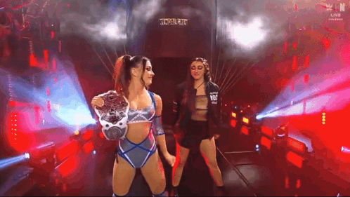 two female wrestlers are standing in a tunnel holding hands and looking at each other .