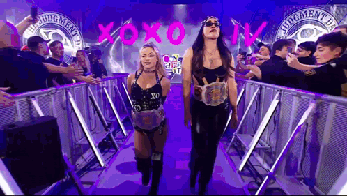 Two Female Wrestlers Are Walking Through A Tunnel With A Crowd Of People Behind Them . GIF
