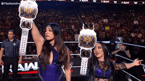 Two Female Wrestlers Hold Up Their Belts In Front Of A Crowd GIF