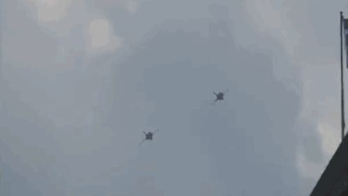 two fighter jets are flying in the sky near a building .