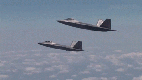 Two Fighter Jets Are Flying Side By Side In A Cloudy Sky GIF