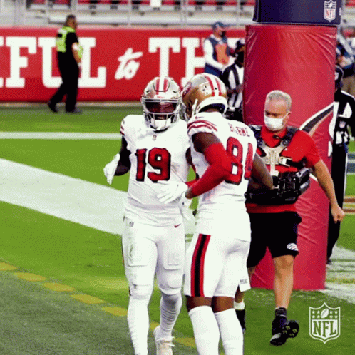 Two Football Players Are Hugging Each Other On A Field With The Nfl Logo In The Background GIF