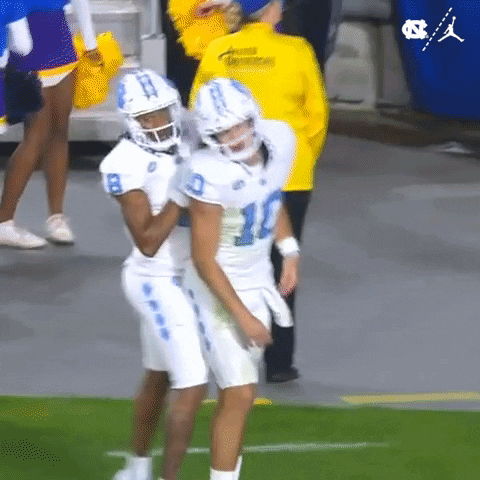 two football players are hugging each other on the field while a cheerleader stands behind them .