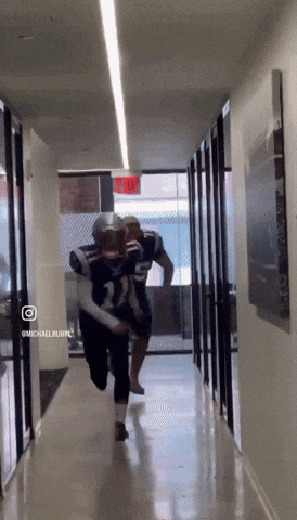 two football players are running down a hallway with a red exit sign behind them