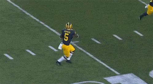two football players are running on the field with the letter m in the background