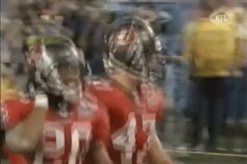 Two Football Players In Helmets Standing Side By Side GIF