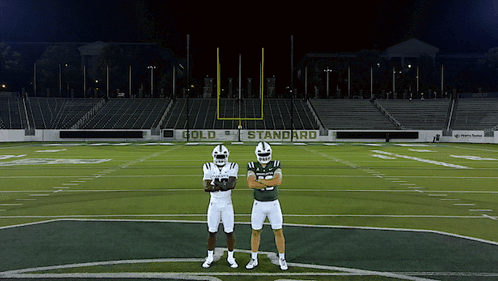 two football players standing on a field with a sign that says gold standard in the background