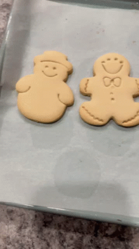 Two Gingerbread Men Are Sitting On A Baking Sheet On Top Of Wax Paper GIF