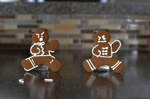 Two Gingerbread Men Standing Next To A Salt Shaker On A Counter GIF