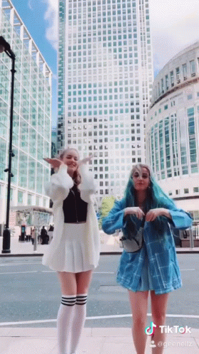 Two Girls Are Dancing In Front Of A Tall Building And A Sign That Says Tiktok On It GIF