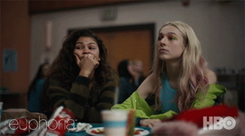 Two Girls Are Sitting At A Table With A Hbo Logo In The Corner GIF
