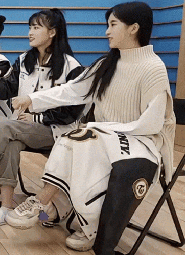 Two Girls Are Sitting In Chairs With One Wearing A Jacket That Says Twice GIF