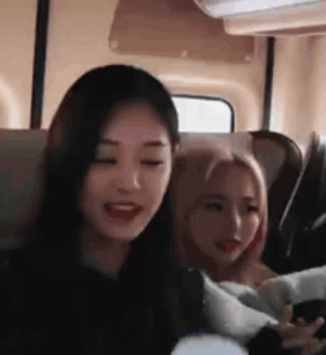 two girls are sitting next to each other on a bus and one of them is holding a cell phone .