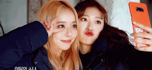 Two Girls Are Taking A Selfie With A Cell Phone That Says B On It GIF