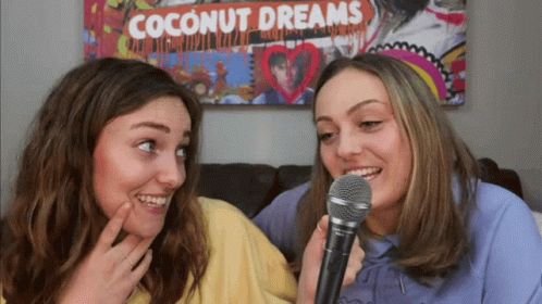 Two Girls Singing Into Microphones In Front Of Coconut Dreams Poster GIF
