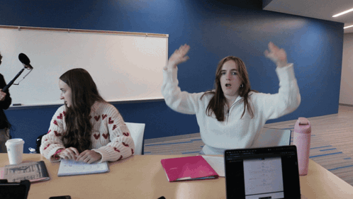 Two Girls Sitting At Table With Arms Up GIF