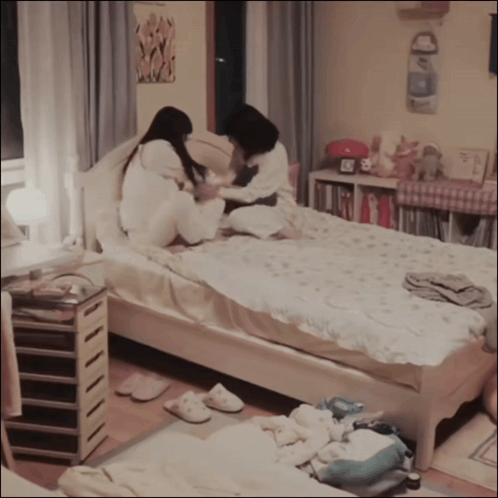 Two Girls Sitting On Bed With Clock GIF