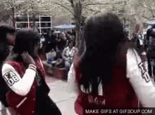Two Girls Wearing Varsity Jackets Are Standing Next To Each Other On A Sidewalk . GIF