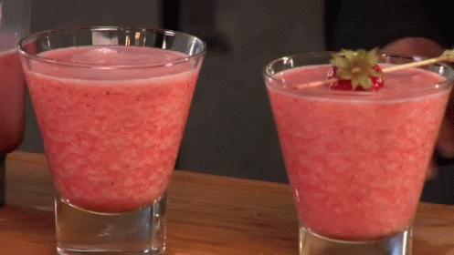Two Glasses Of Pink Liquid With A Strawberry On A Stick GIF