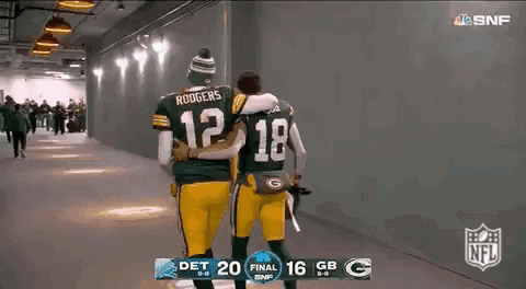 two green bay packers players are hugging each other while walking down a hallway .