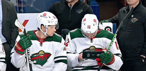 Two Hockey Players Are Looking At Their Phones While Sitting In The Stands GIF