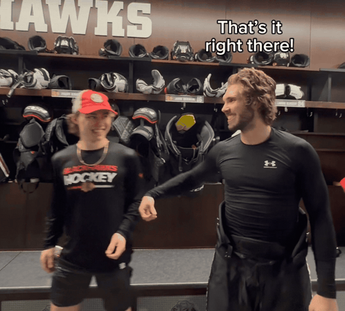 Two Hockey Players In A Locker Room That Says Hawks On The Wall Behind Them GIF