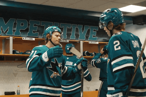 Two Hockey Players In A Locker Room With A Banner Behind Them That Says ' Competitive ' GIF