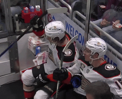 Two Hockey Players Sitting In Front Of A Sign That Says Welcom GIF