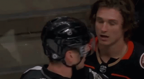 Two Ice Hockey Players Are Talking To Each Other While Wearing Helmets . GIF