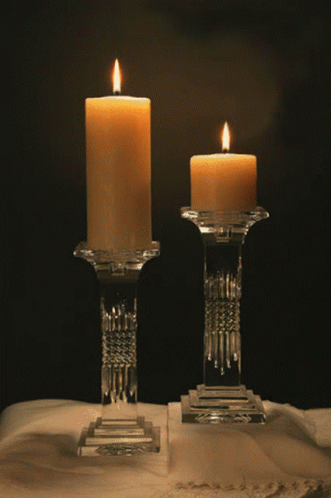 Two Lit Candles In Clear Glass Holders On A Table GIF