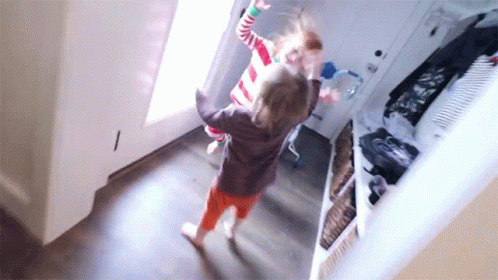 Two Little Girls Are Dancing In A Hallway In Front Of A Door . GIF