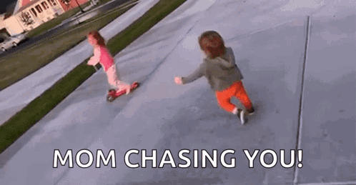Two Little Girls Are Riding Scooters On A Sidewalk And The Words `` Mom Chasing You '' Are Visible . GIF