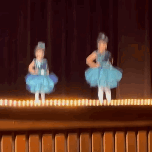 Two Little Girls In Blue Dresses Are Dancing On A Stage . GIF