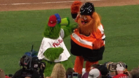 Two Mascots From The Phillies Are Standing On A Baseball Field GIF