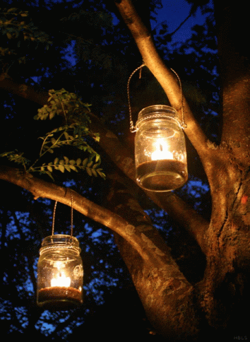 Two Mason Jars With Candles Hanging From Tree GIF