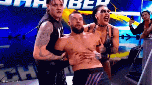 Two Men And A Woman Are Holding A Shirtless Wrestler In A Ring . GIF