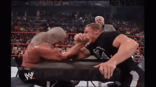Two Men Are Arm Wrestling In A Wrestling Ring With A Referee Watching . GIF