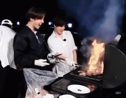 Two Men Are Cooking Food On A Grill With Flames . GIF