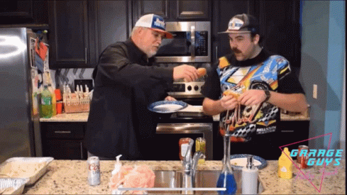 Two Men Are Cooking In A Kitchen And One Has A Shirt That Says Grand Guys On It GIF
