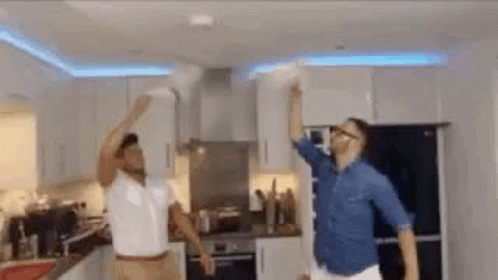 Two Men Are Dancing In A Kitchen In Front Of A Fire Alarm . GIF