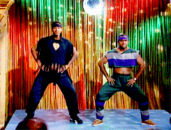Two Men Are Dancing In Front Of A Colorful Curtain GIF