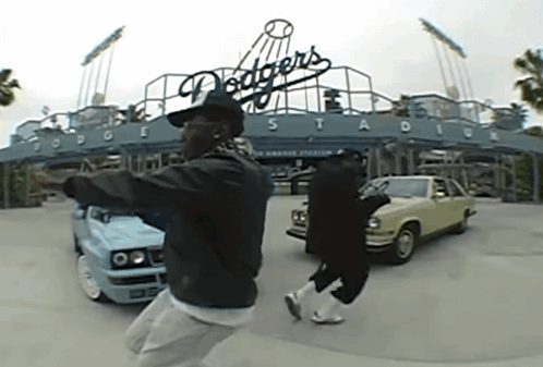 Two Men Are Dancing In Front Of A Dodgers Stadium Sign GIF