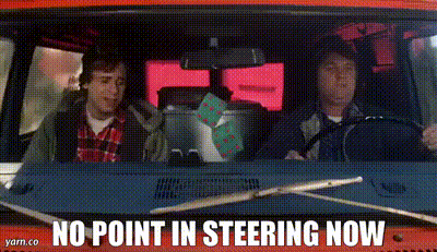 two men are driving a red van with the words `` no point in steering now '' on the dashboard .
