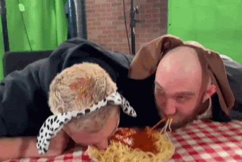 Two Men Are Eating Spaghetti Together On A Checkered Table Cloth . GIF