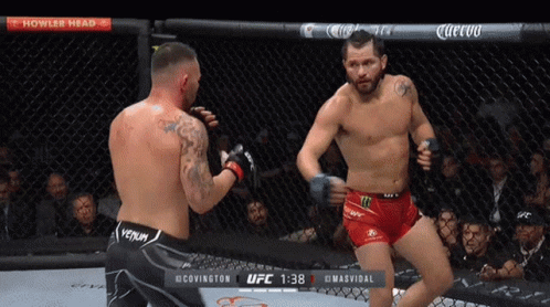 Two Men Are Fighting In A Cage With A Sign That Says Howler Head Above Them GIF