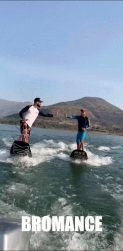 Two Men Are Giving Each Other A High Five While Riding A Wave On A Body Of Water With The Word Bromance Below Them GIF