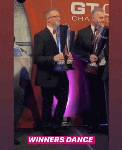 Two Men Are Holding Trophies In Front Of A Sign That Says Winners Dance GIF